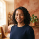 A friendly, diverse woman smiling confidently in a bright, modern studio with warm-toned decor.